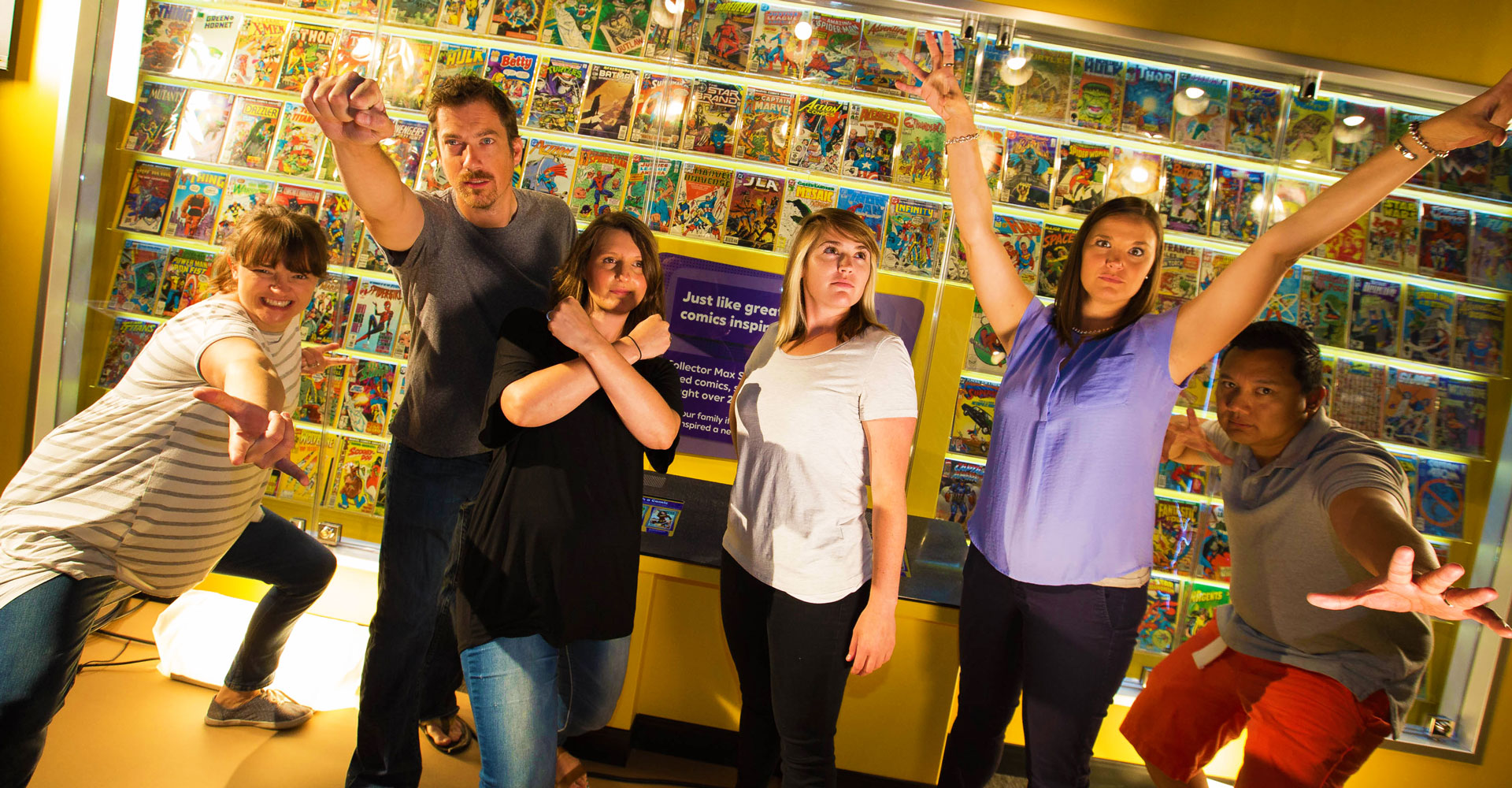 Adults in superhero poses with a wall of comic books behind them.
